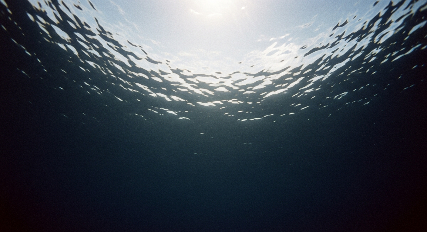 Dark water surface from underwater looking up, light rippling and refracting from far above, deep blue-black depth below