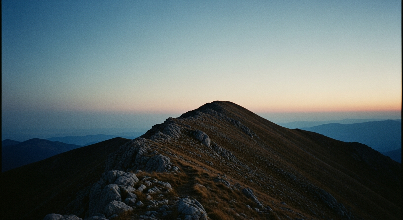 Pre-dawn mountain ridgeline against a deep blue-black sky, faint gray light beginning at the horizon