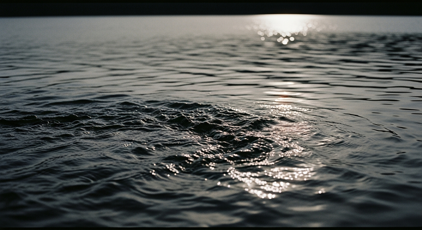 Dramatically textured dark water surface with one sharp line of silver light at the horizon, disturbed surface gradually calming toward frame edge